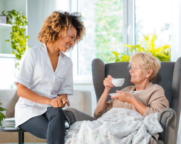 Home caregiver providing compassionate in-home care and companionship to an elderly woman in a comfortable living room setting.